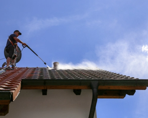 Technician power washing a commercial building roof to remove buildup