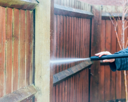Worker pressure washing a weathered wood deck to restore its surface