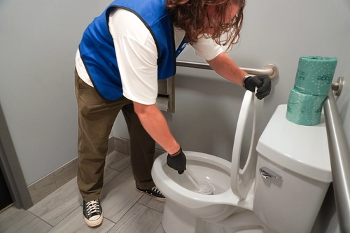Worker scrubbing a shared office restroom toilet during routine upkeep